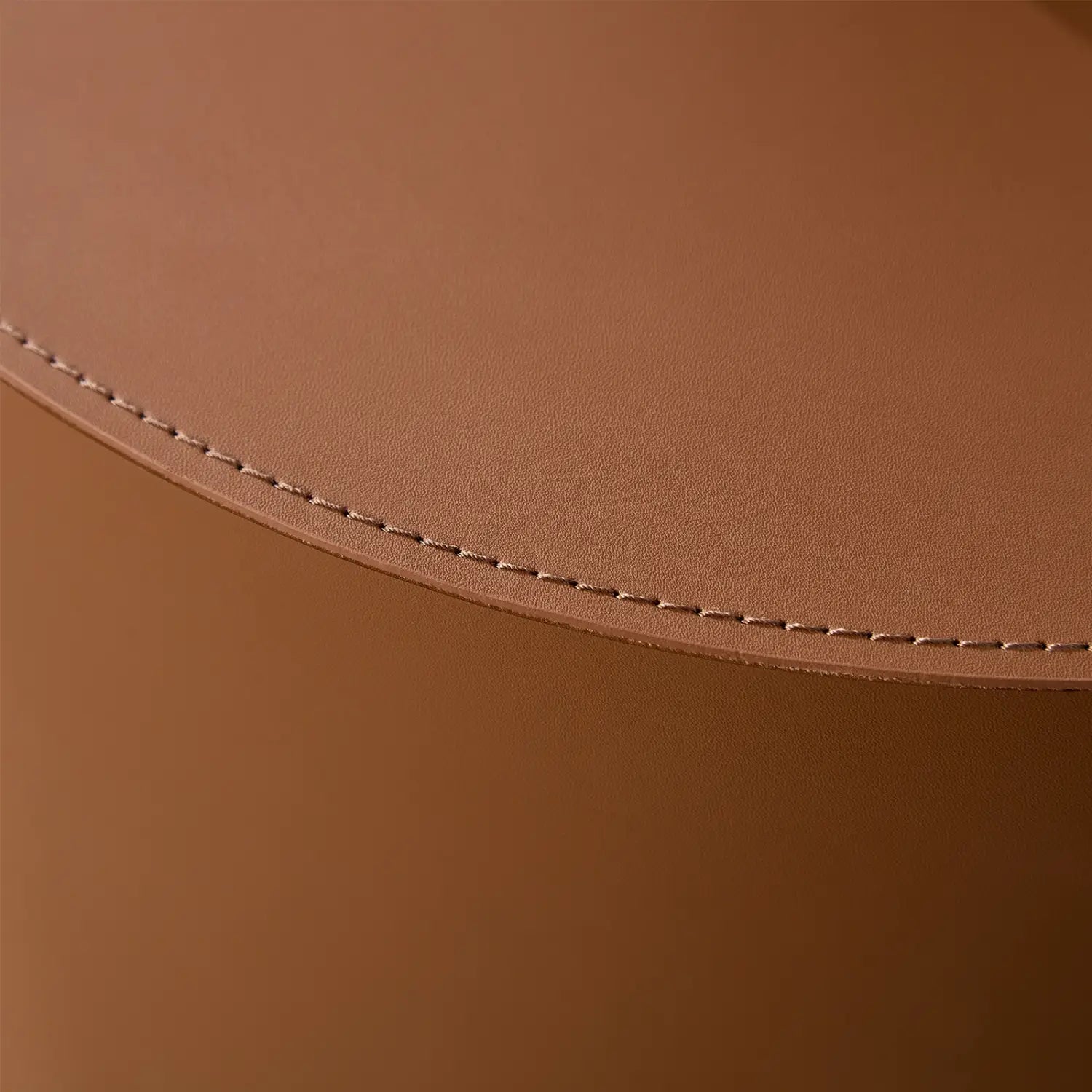 Juego de mesa de centro cilíndrica de cuero marrón tipo silla de montar, con un posavasos redondo de cuero color canela y costuras precisas a juego a lo largo del borde curvado