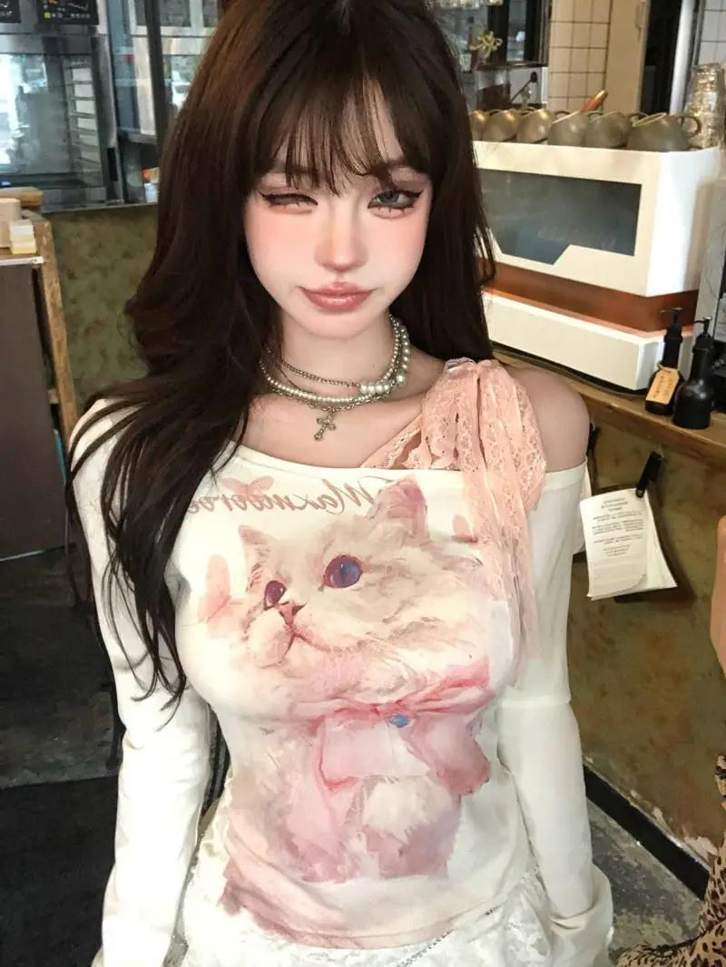 A white long-sleeved top featuring a detailed pink cat illustration with purple eyes and a bow accented by lace detailing on the shoulder in the cat print lace halter long sleeve top.