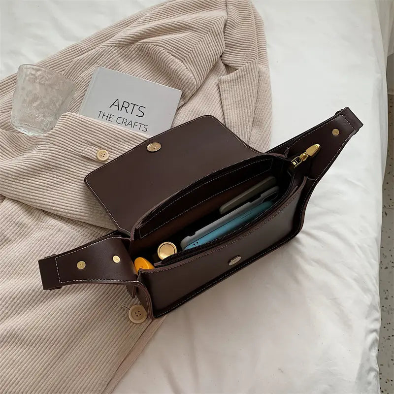 Brown leather crossbody bag with gold-tone hardware and button closures designed as a minimalist shoulder purse.