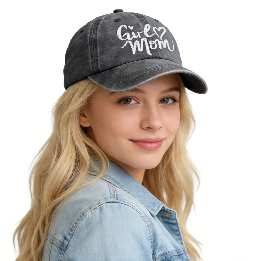Une casquette de baseball grise foncée à l’aspect vieilli avec « girl mom » brodé en blanc en script cursif, comportant une sangle réglable.