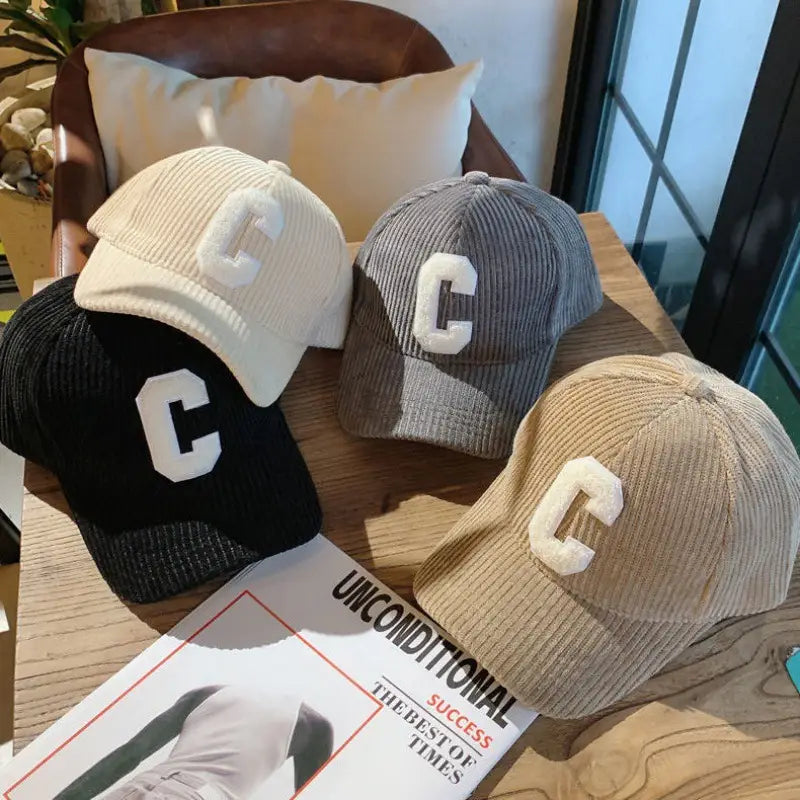 three corduroy baseball caps in cream gray and black featuring a prominent white embroidered c on the front.