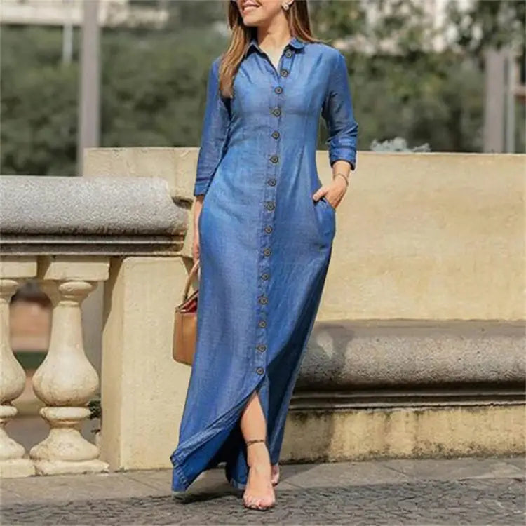A long blue denim button front maxi dress with long sleeves and a side slit.