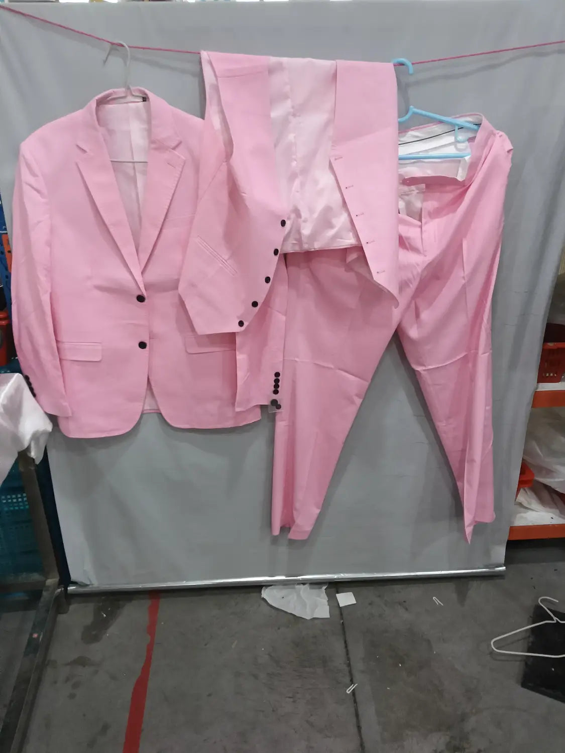 Un costume deux pièces en lin rose avec boutons noirs et doublure satin, suspendu sur des cintres, conçu comme tenue décontractée pour marié, banquet, coupe slim