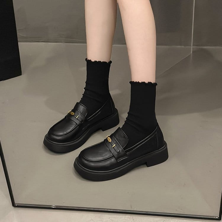 black leather loafers with a thick sole and gold tone buckle accents displayed from the back side
