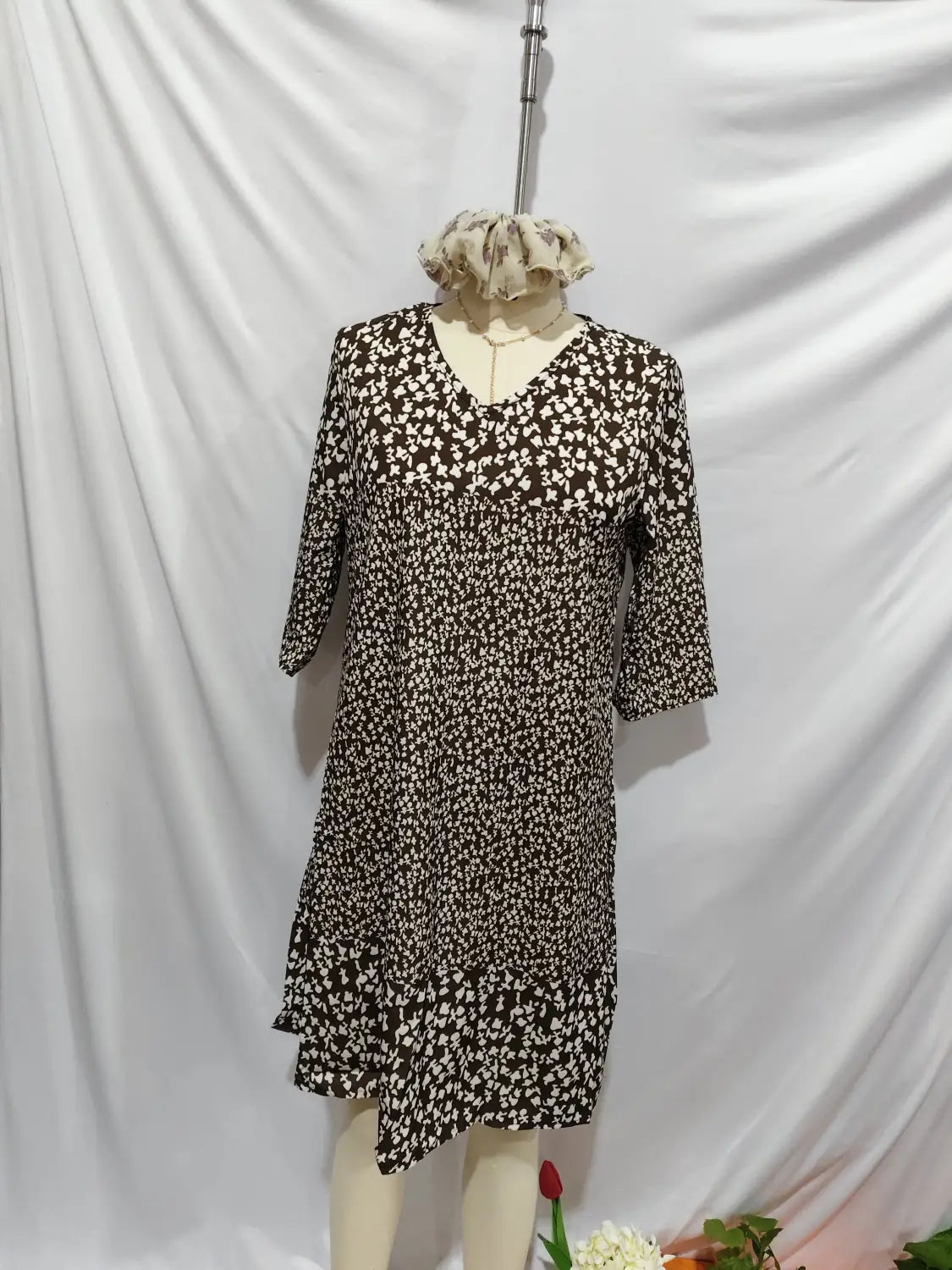 Une robe midi à imprimé floral marron et blanc, avec une encolure en V, des manches trois-quarts et un ourlet asymétrique.