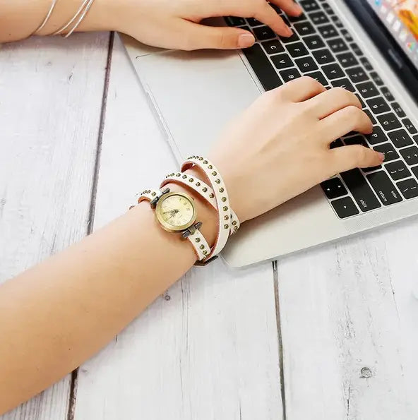 A vintage leather studded wrap watch bracelet featuring a delicate cream-colored leather strap with silver-toned studs and a round vintage-style face.
