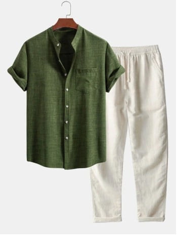 Ensemble chemise pour homme à manches courtes et pantalon comprenant une chemise kaki olive à manches courtes boutonnée, avec un tissage légèrement texturé et une poche poitrine unique, présentée sur un cintre en bois à côté d’un pantalon blanc assorti à cordon de serrage.