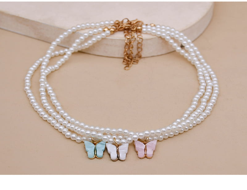 An elegant pearl butterfly charm choker necklace featuring a delicate triple-strand design with three pastel butterfly charms in light blue white and pink.