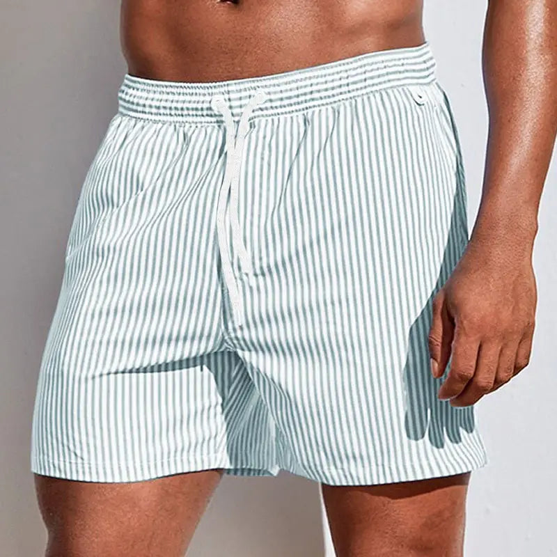 Men’s striped tropical print swim trunks featuring light blue and white vertically striped fabric with an elastic waistband.