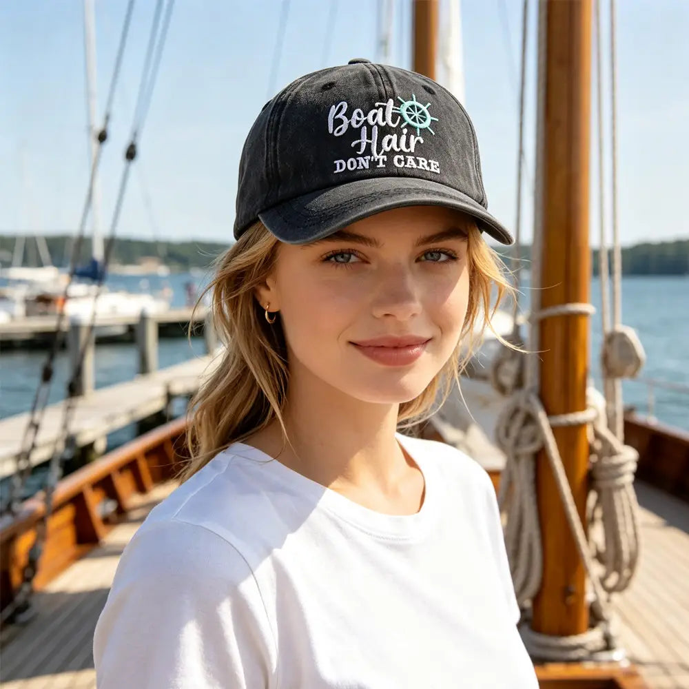 Black baseball cap made of fabric with white and teal embroidered text reading boat hair don’t care on the front.