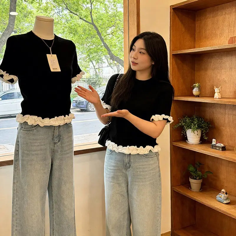 Black short-sleeved knit top featuring white ruffled trim at the cuffs and hem designed for stylish casual wear.