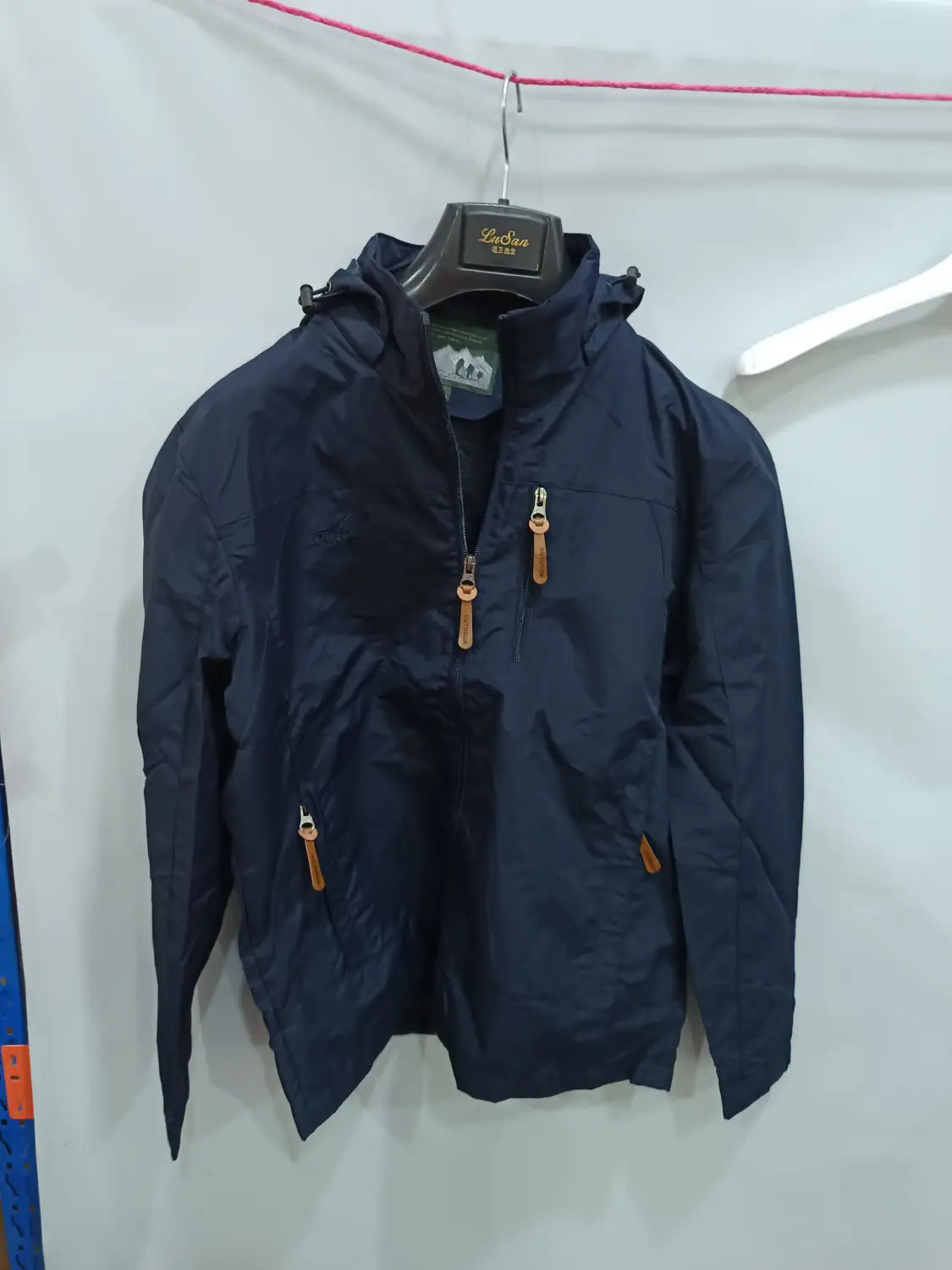 Chaqueta de senderismo con capucha impermeable color azul marino oscuro, con tiradores de cremallera de cuero color camel y una etiqueta de marca sutil en el cuello.
