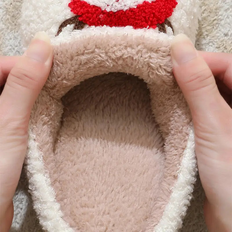 A cozy plush beige and white fuzzy festive embroidered Santa and reindeer winter slipper with a red bow detail on top.