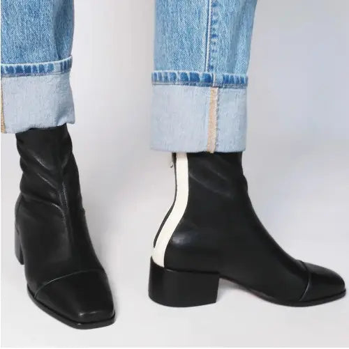 Die Rückseite schwarzer Stiefeletten aus Leder mit eckiger Zehenpartie mit kontrastierendem weißem Streifen als Reißverschlussdetail.
