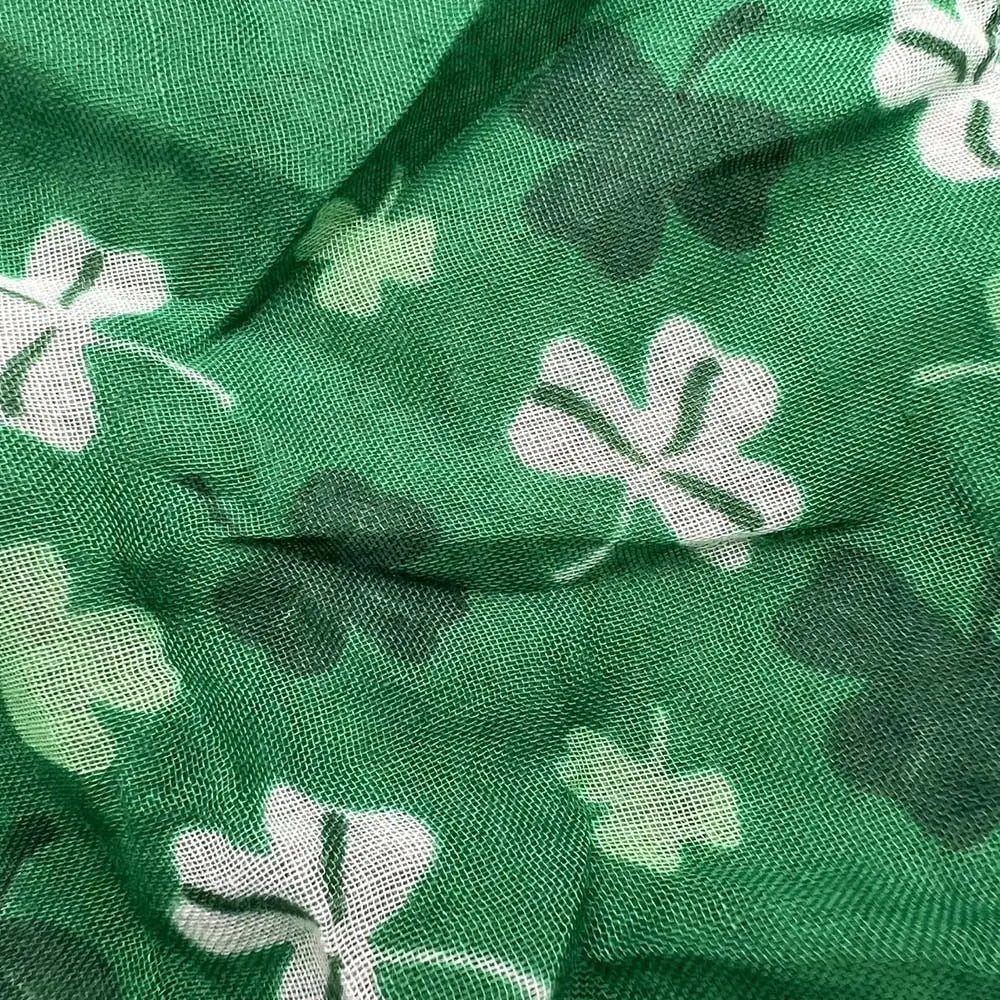 Un foulard à motif de trèfle vert imprimé, fabriqué dans un tissu présentant un motif de trèfles blancs et vert foncé, dans des tonalités vert terre.