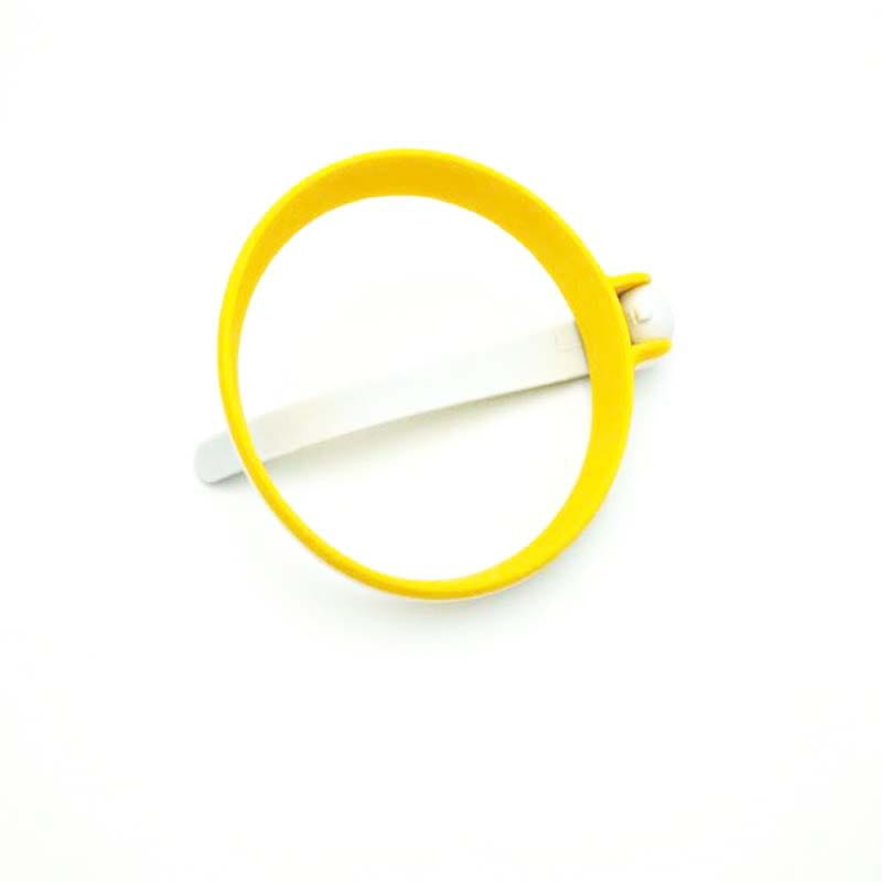 Gelbes Kunststoff-Armband mit weißem Riemen und Schnalle, das neben einem Silikon-Eierring für einen runden Omelettform mit Griff zur Zubereitung dargestellt ist.