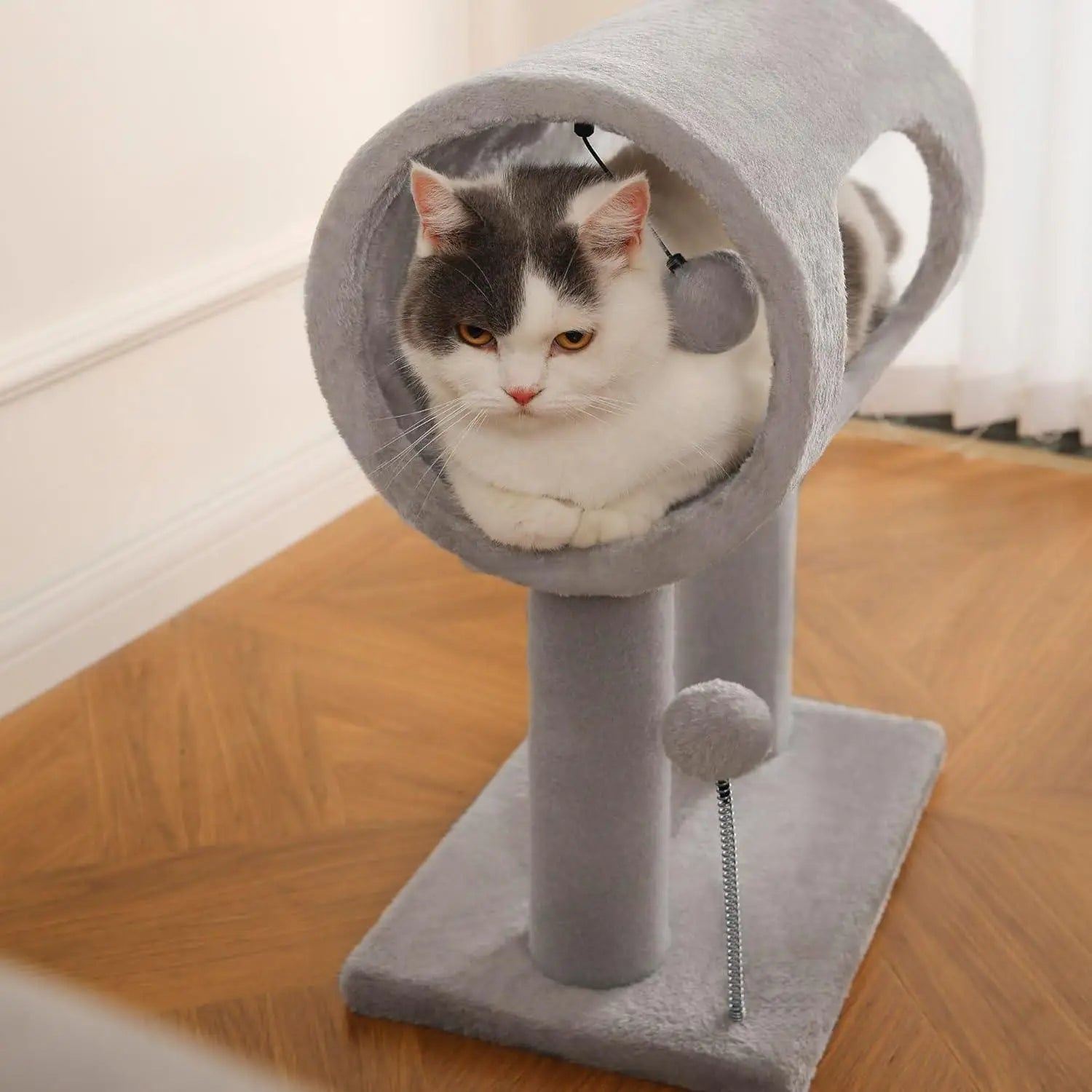 Gray plush cat tree with tunnel and scratching post featuring a dangling ball toy for feline entertainment.