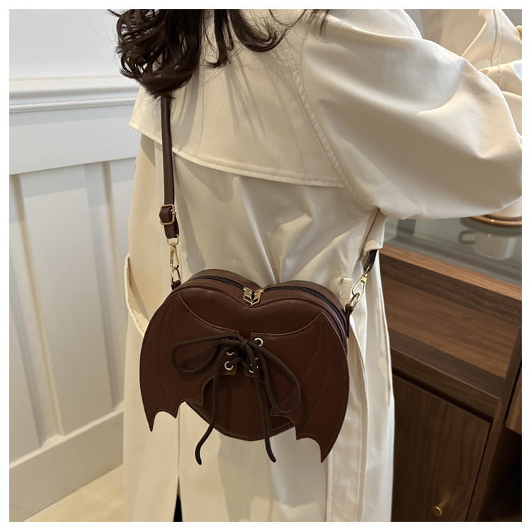 Brown bat-shaped crossbody bag featuring lace-up front detail and gold-tone hardware.