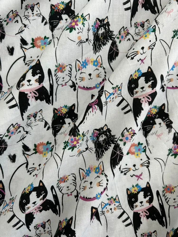 White vintage 1950s cotton dress featuring a repeating pattern of black and white cats with colorful floral crowns