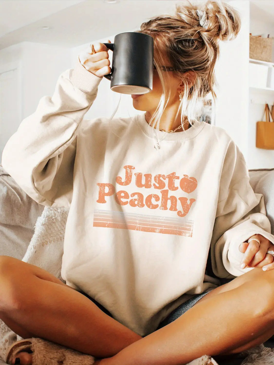 Sudadera extragrande de color crema confeccionada con material suave, con «just peachy» impreso en color naranja desvaído, en una tipografía retro, a lo largo del pecho.