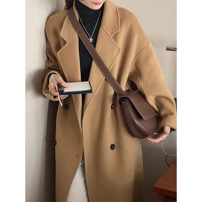 Brown leather crossbody bag with a curved minimalist design and single shoulder strap featured with a pink longline wool trench coat petite.