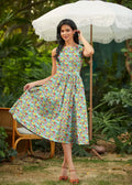 A woman wears a light green farmer’s market floral cotton retro midi dress with pockets and vibrant red yellow purple flowers