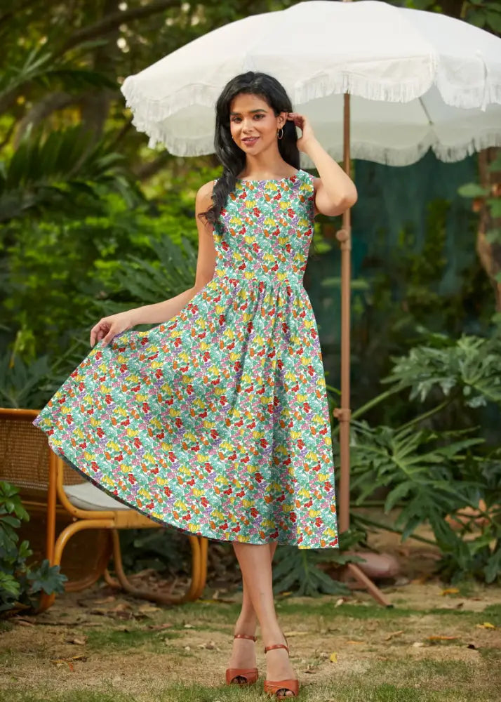 A woman wears a light green farmer’s market floral cotton retro midi dress with pockets and vibrant red yellow purple flowers