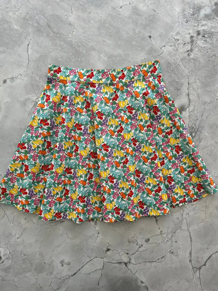 A vibrant cotton skater skirt with pleated colorful fruit and berry print on white background farmers market style
