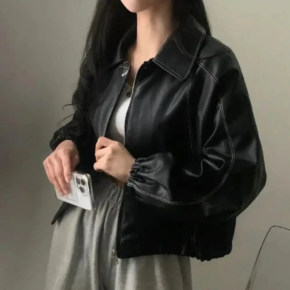 Black faux leather bomber jacket with contrast white stitching and elasticized cuffs shown from the front