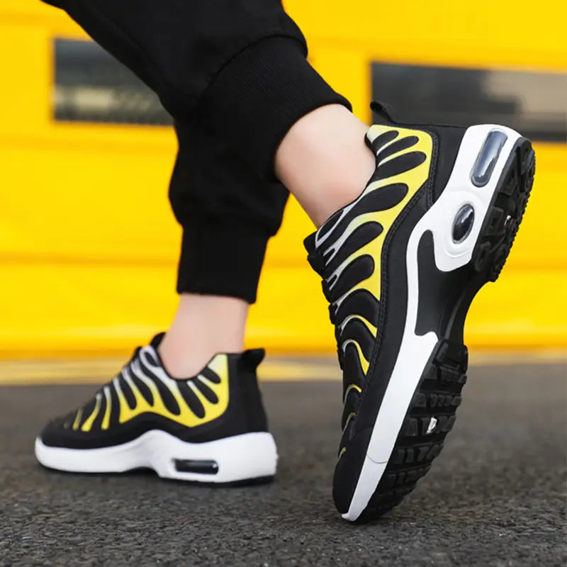 Black and yellow Nike Air Max Plus air cushion running shoes featuring a bold flame-like pattern on the side with a white midsole and visible air cushioning units.