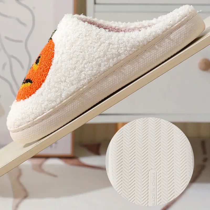 White plush jack-o-lantern embroidered halloween slippers featuring an orange pumpkin face on the side.