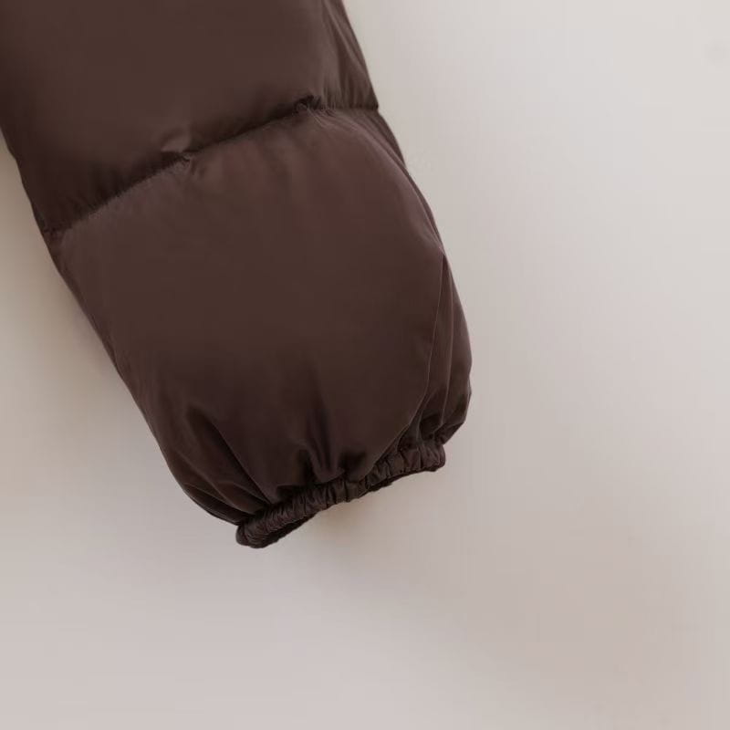 Detailaufnahme des Ärmelbündchens von einem dunkelbraunen wattierten Steppmantel mit elastischer Einfassung, ausgelegt für Wärme im Winter.