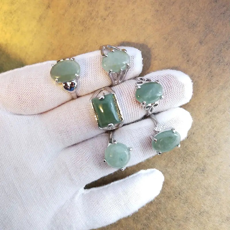 A collection of five natural gemstone silver tone statement rings featuring green jadeite stones in oval and rectangular shapes with silver toned metal settings.