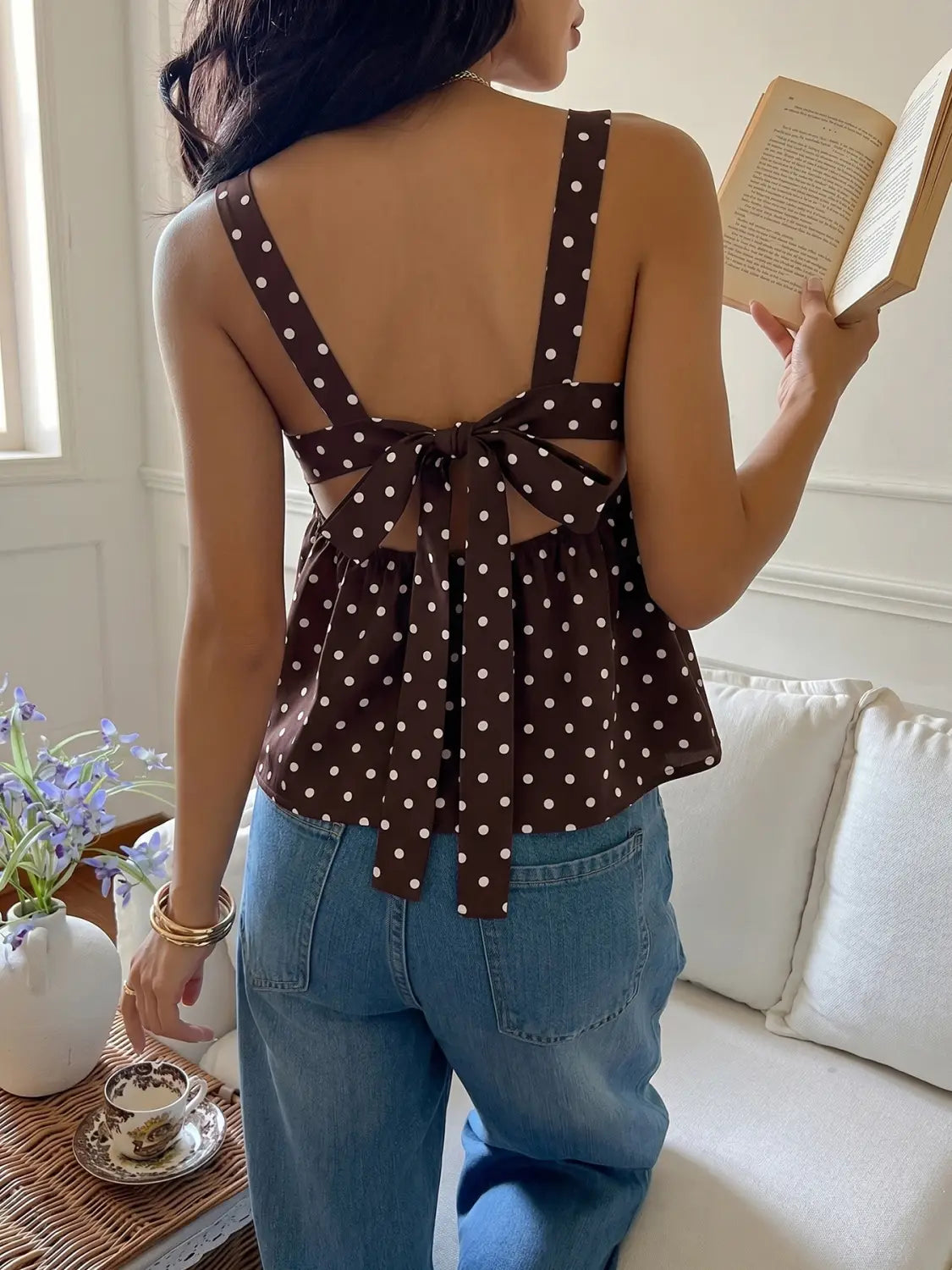 brown polka dot peplum camisole showing the back side with a tied bow at the center on a lightweight fabric.