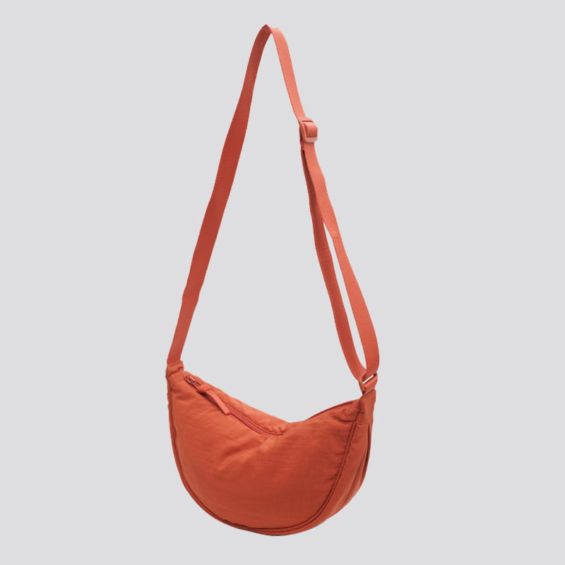 A sleek rust-orange nylon dumpling messenger bag with a curved crossbody strap featuring subtle stitching details.