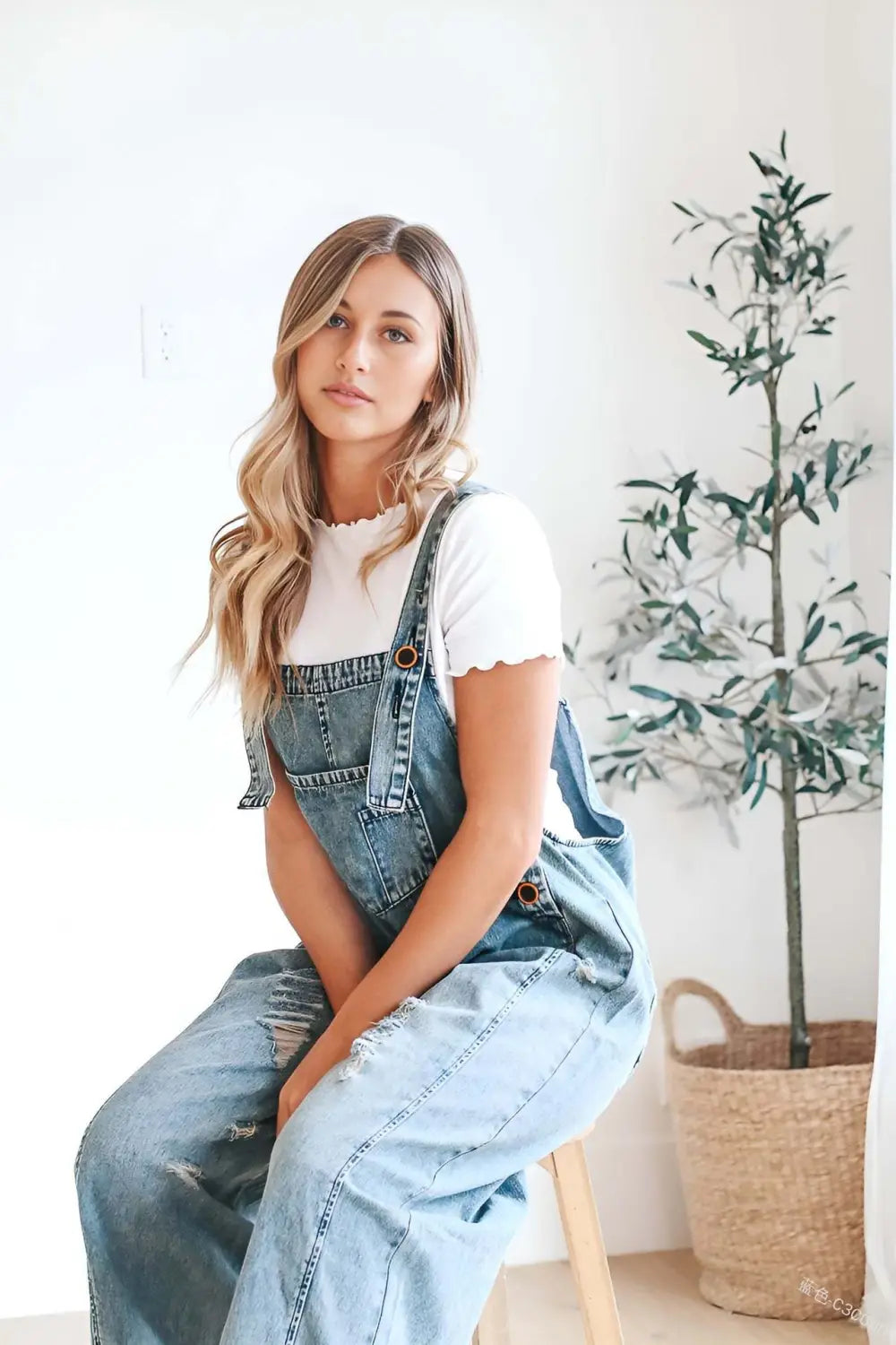 Women’s light-wash distressed denim overalls with adjustable straps frayed hem and button closures.