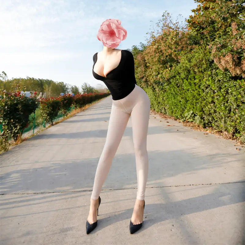 A person wearing sheer high waisted beige leggings made of sheer material paired with a black fitted top and black high heels with their face obscured by a large pink flower.