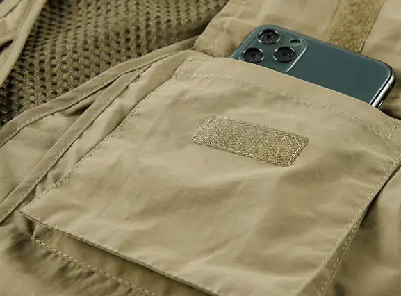 Une poche de gilet utilitaire en mesh à séchage rapide de couleur kaki, avec un empiècement en tissu beige et des coutures cousues maintenant un smartphone vert foncé