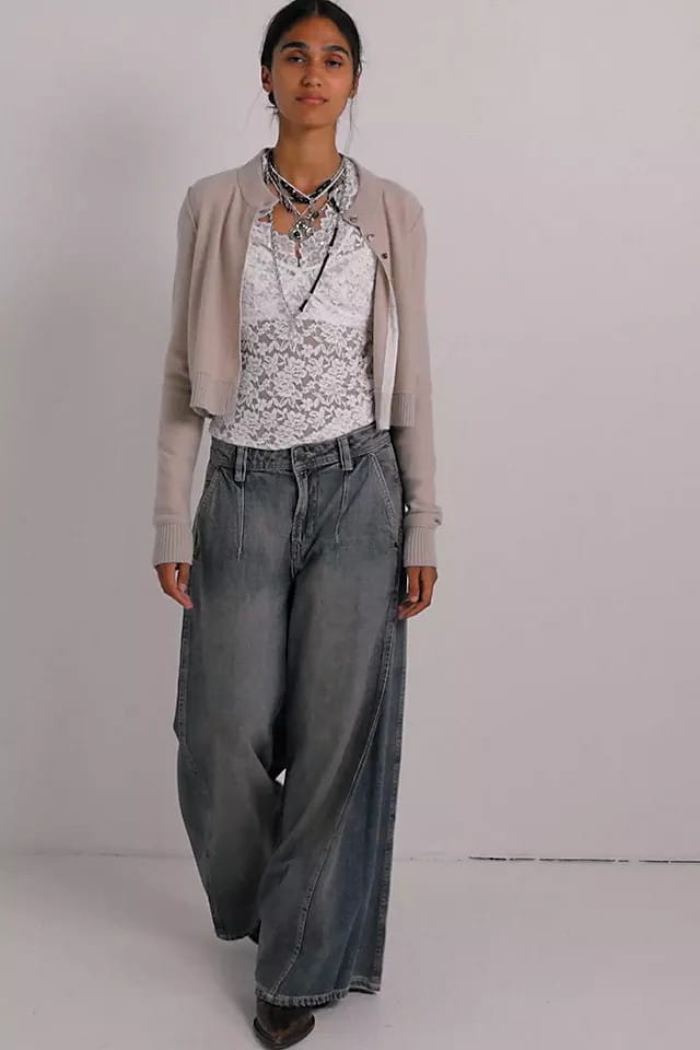 Una mujer lleva vaqueros retro de mezclilla de pierna ancha en azul vintage combinados con una chaqueta tipo cárdigan corta beige y una blusa blanca de encaje.
