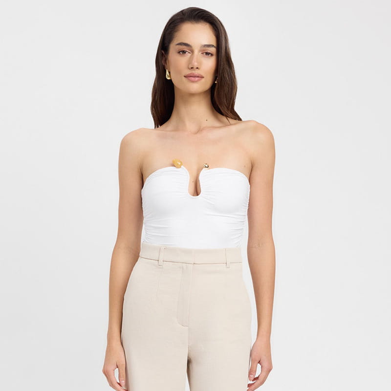 White strapless keyhole crop top bodysuit with a central cutout and gold-tone button accents.