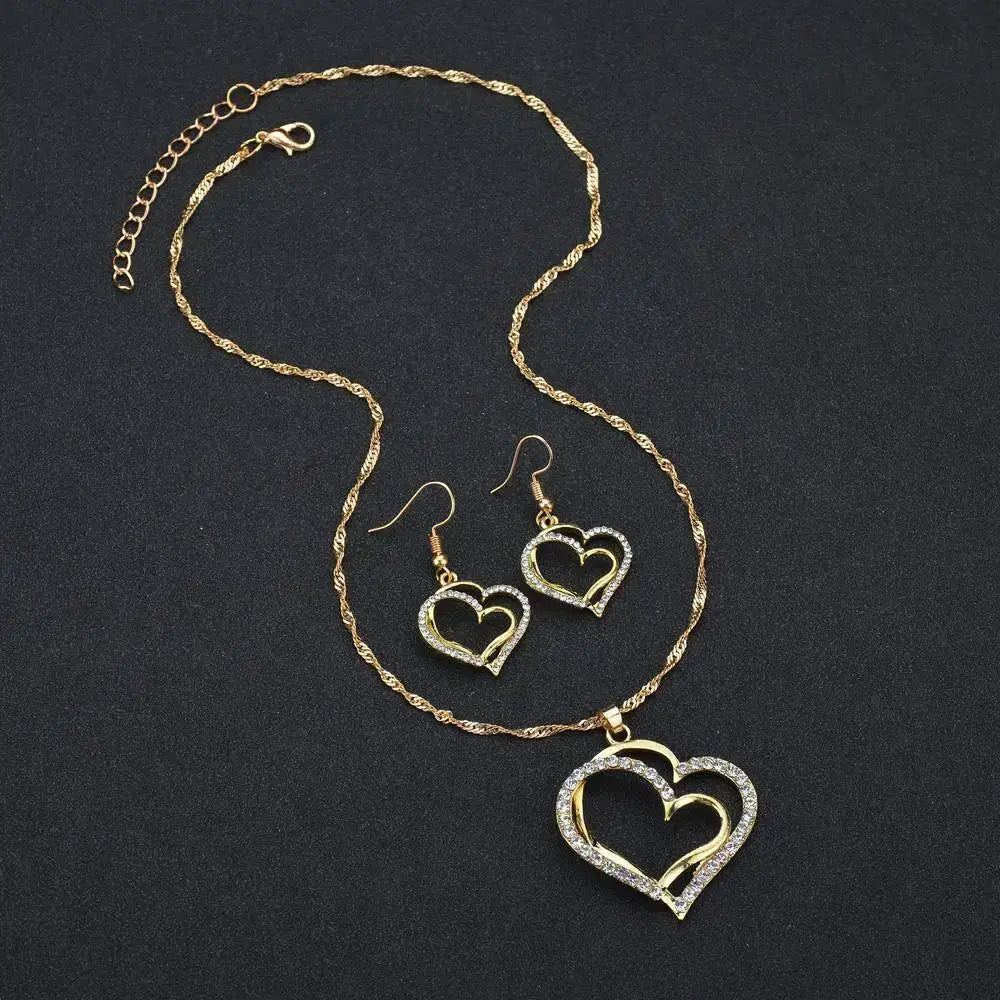 Elegant rhinestone heart jewelry set featuring a gold-toned heart-shaped necklace with a twisted chain and matching openwork earrings adorned with sparkling rhinestones.