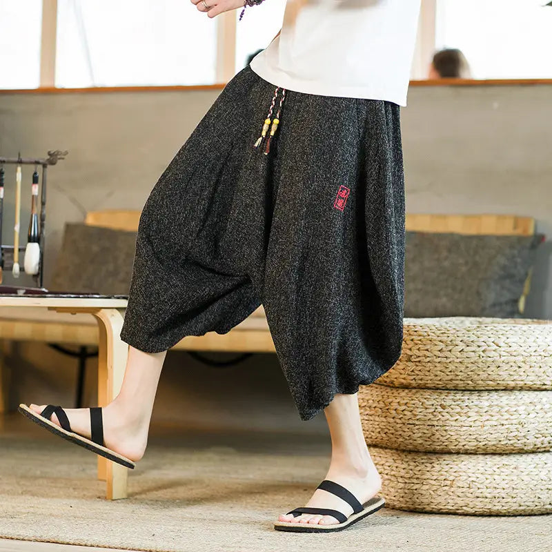 Herren-Shorts aus schwarzem bedrucktem Baumwollstoff im Lantern-Harem-Look mit weitem Bein, mit kleinem rotem besticktem Patches an der Oberschenkelpartie.