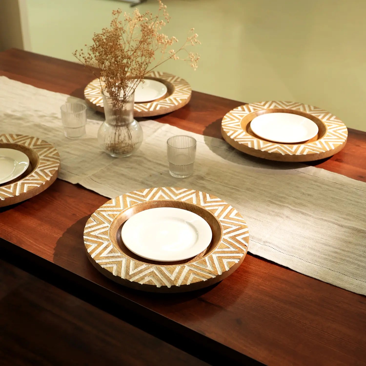 Juego de cuatro platos portavelas de madera artesanales de 13 pulgadas, con acabado de madera natural y patrones de incrustación geométrica blanca intrincados alrededor del borde, cada uno con un plato central de cerámica blanca.