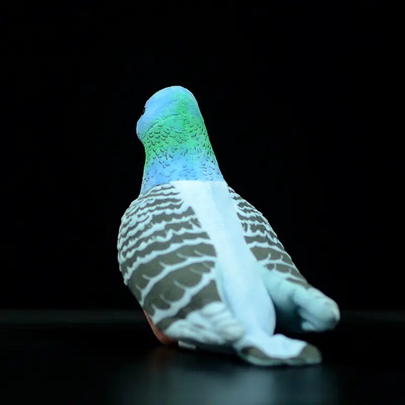Une peluche de colombe multicolore brillante de 19 cm, avec une tête bleue et verte, un corps blanc et des motifs de plumes gris, conçus comme une poupée d’oiseau