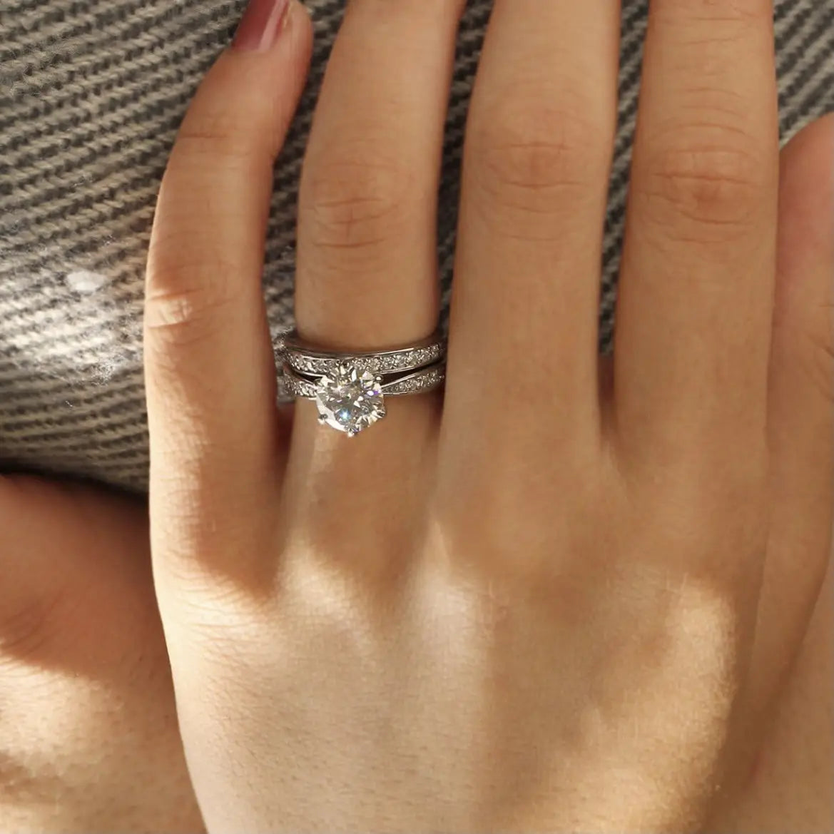 A sparkling silver round cut zircon engagement ring set in white gold finish with a central round-cut diamond and a band adorned with smaller diamonds worn on a finger.