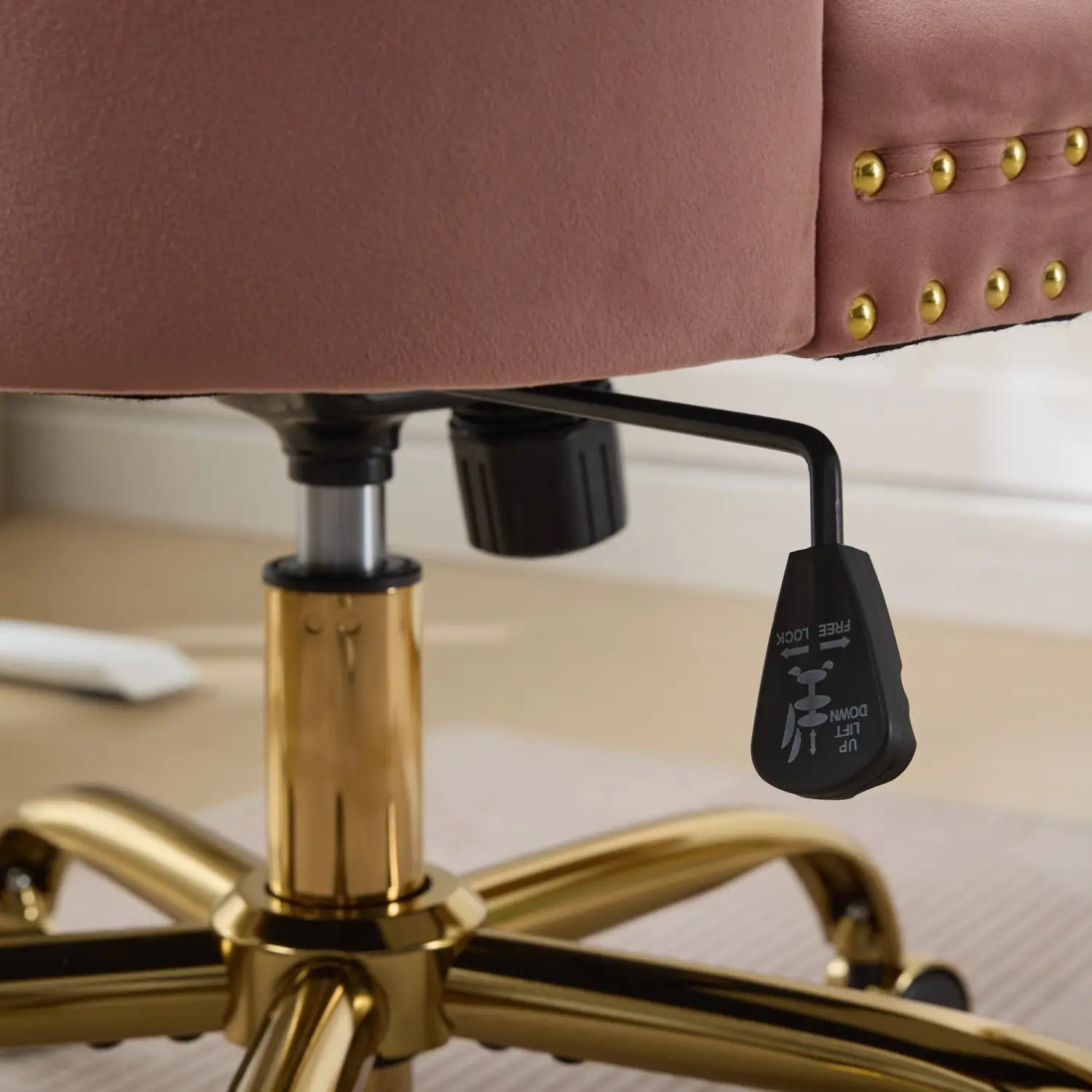 Un fauteuil de bureau moelleux en velours rose poudré, capitonné, avec des accents métalliques ton doré et des clous décoratifs en laiton le long du bord.