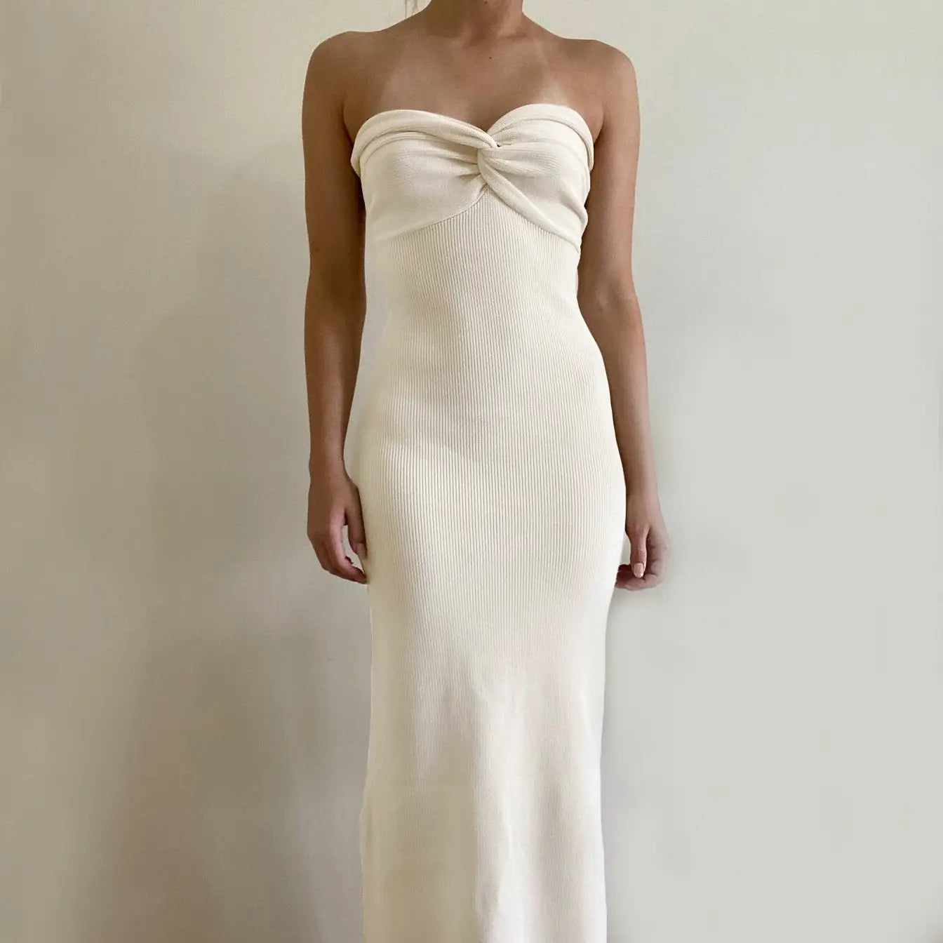 Cream-colored off shoulder knotted ribbed knit midi dress with strapless design and twisted knot detail at the bust.