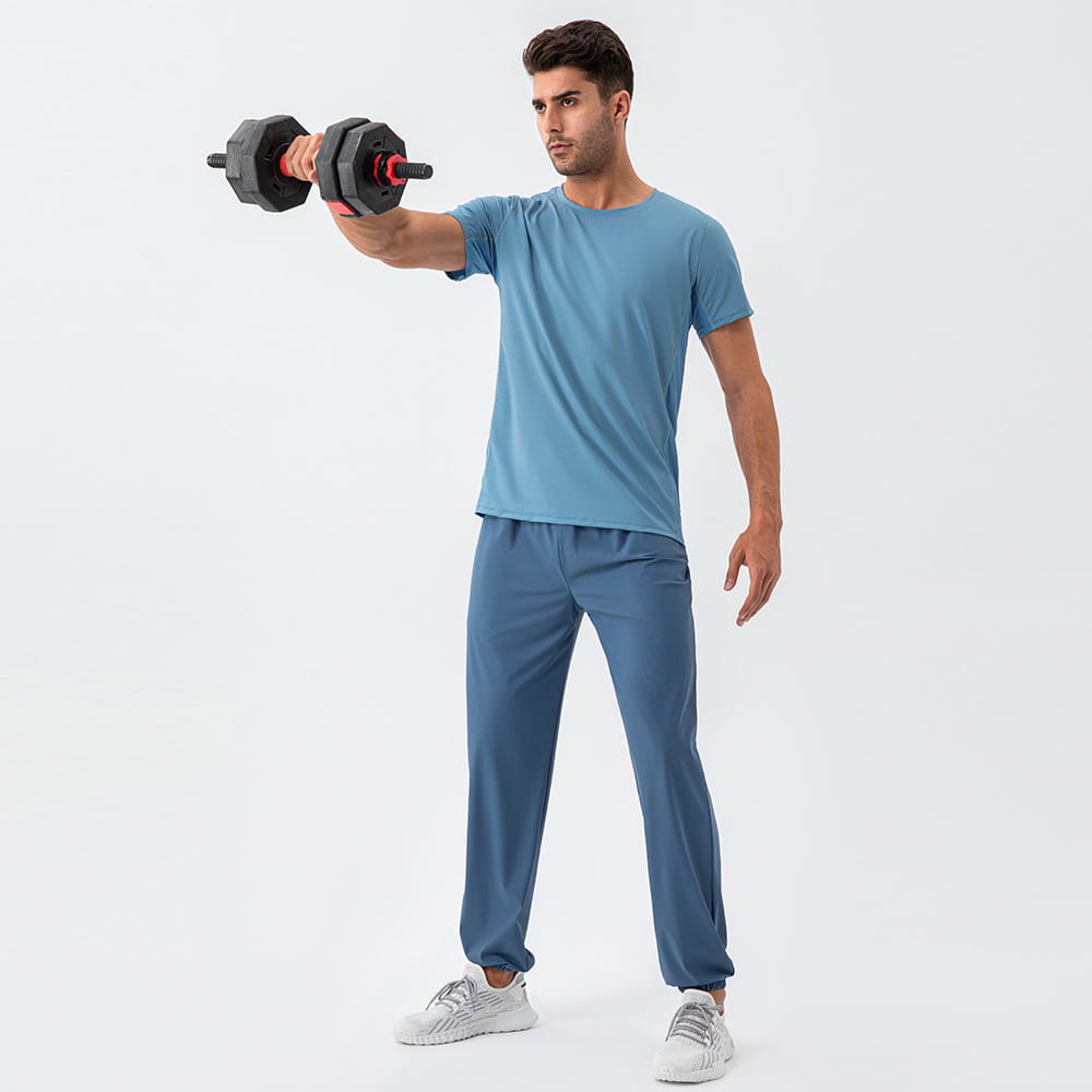 man wearing blue quick dry nylon loose fit athletic track pants holding a black and red dumbbell