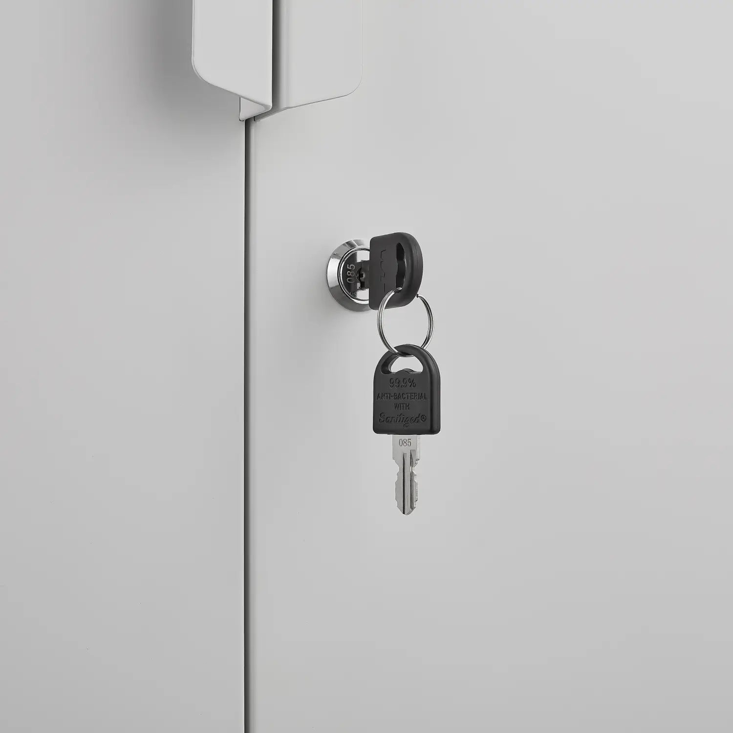 Black plastic key with a silver metal blade inserted in a circular chrome lock on a white steel file cabinet 70 inch 2 door lockable storage door.