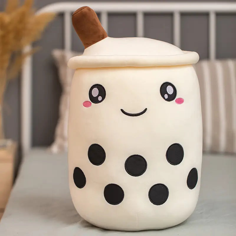 Cute cream-colored plush boba milk tea cup with black embroidered tapioca pearls and facial features made of soft fabric, featuring a brown straw on top as a stuffed hugging pillow.